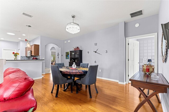 9551 SW 92nd Ter, Ocala, FL 34481 - dining space with arched walkways, light wood-style flooring, a chandelier, baseboards, and a textured ceiling
