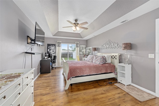 63 Walnut Crse, Ocala, FL 34480 - bedroom with a tray ceiling, light wood-style flooring, baseboards, a ceiling fan, and a textured ceiling