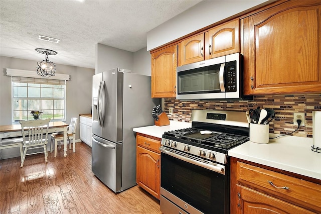 986 SE 57th Ave, Ocala, FL 34480 - kitchen featuring stainless steel appliances, brown cabinetry, light wood finished floors, backsplash, and a textured ceiling