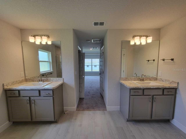 15055 SW 25th Cir, Ocala, FL 34473 - full bathroom featuring wood finished floors, two vanities, a textured ceiling, baseboards, and a textured wall