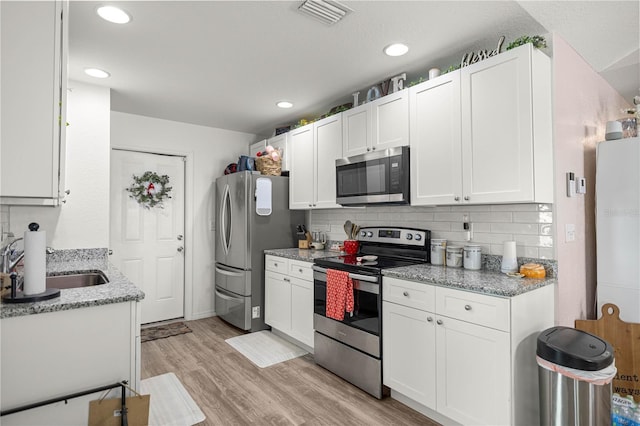 5063 SE 168th Ter, Ocklawaha, FL 32179 - kitchen featuring stainless steel appliances, a sink, white cabinetry, tasteful backsplash, and light wood-type flooring