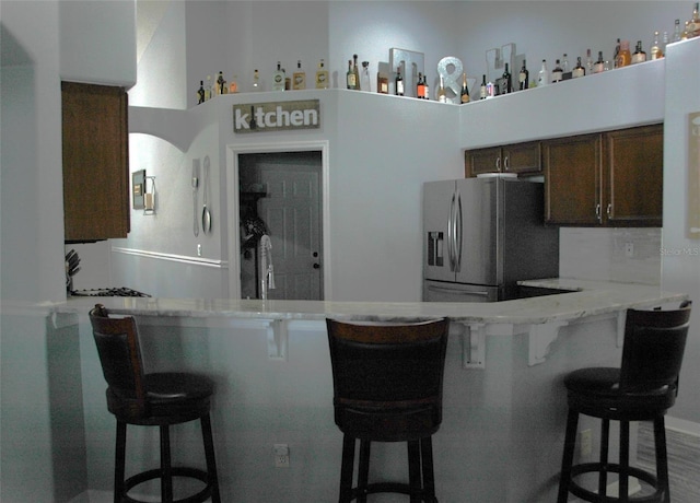 14126 Greater Pines Blvd, Clermont, FL 34711 - kitchen with stainless steel fridge with ice dispenser, dark brown cabinetry, a peninsula, and a kitchen bar