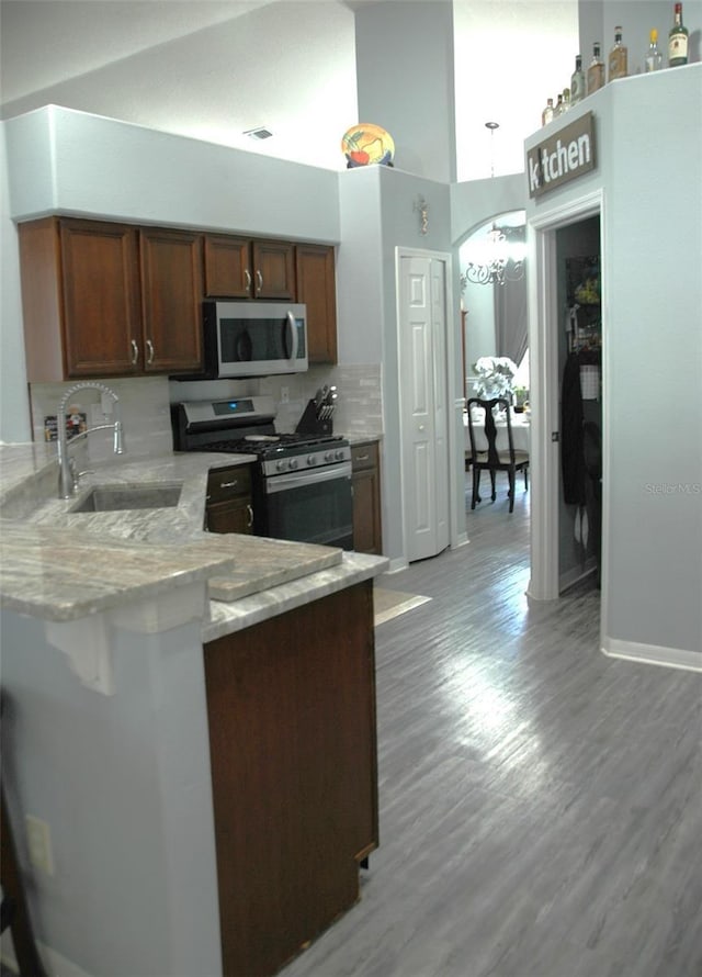 14126 Greater Pines Blvd, Clermont, FL 34711 - kitchen featuring appliances with stainless steel finishes, a sink, a peninsula, light stone counters, and light wood-type flooring