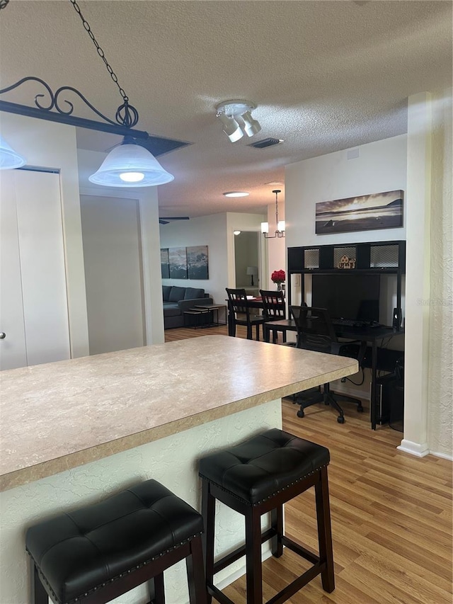 9255 SW 90th Ct Unit B, Ocala, FL 34481 - kitchen with a textured ceiling, light wood-style floors, pendant lighting, a breakfast bar, and baseboards