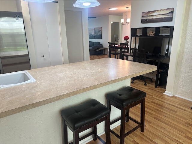 9255 SW 90th Ct Unit B, Ocala, FL 34481 - kitchen featuring a textured wall, a kitchen breakfast bar, light wood-style floors, decorative light fixtures, and light countertops