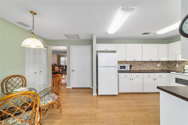 8431 SW 93rd Pl Unit F, Ocala, FL 34481 - kitchen with white appliances, dark countertops, light wood-style floors, white cabinets, and hanging light fixtures