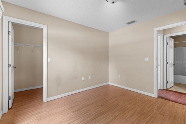 23340 NW Columbine Ave, Dunnellon, FL 34431 - unfurnished bedroom with light wood-type flooring, a closet, a walk in closet, baseboards, and a textured ceiling