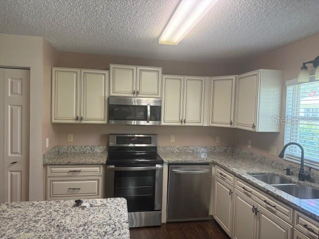 9722 SW 95th Ct Unit C, Ocala, FL 34481 - kitchen with stainless steel appliances, a textured ceiling, dark wood-type flooring, light stone countertops, and white cabinets