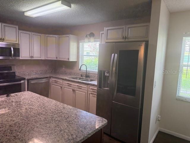9722 SW 95th Ct Unit C, Ocala, FL 34481 - kitchen with appliances with stainless steel finishes, a textured ceiling, healthy amount of natural light, white cabinetry, and light stone countertops
