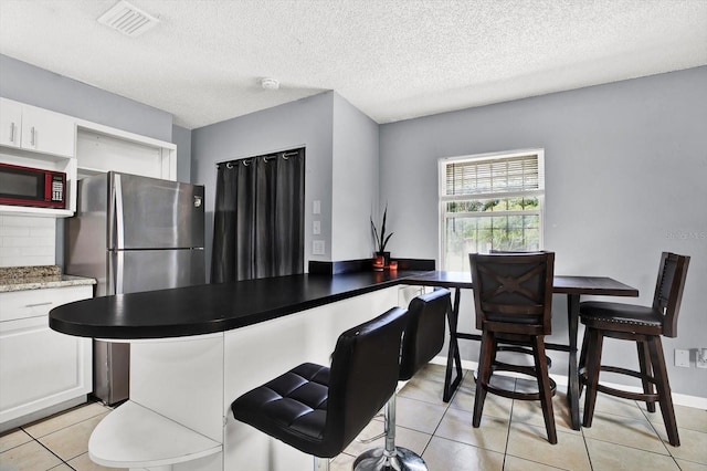 6816 Thomas Cir, Tampa, FL 33619 - kitchen featuring light tile patterned floors, white cabinets, a kitchen bar, a textured ceiling, and freestanding refrigerator