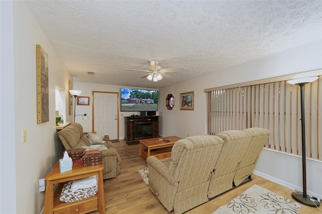 3427 SE 137th St, Summerfield, FL 34491 - living room featuring ceiling fan, light wood-type flooring, a textured ceiling, and a glass covered fireplace