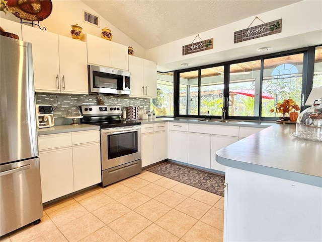 502 SE Guava Ter, Port St Lucie, FL 34983 - kitchen featuring stainless steel appliances, vaulted ceiling, backsplash, a textured ceiling, and white cabinetry