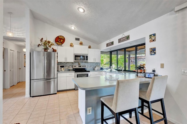 502 SE Guava Ter, Port St Lucie, FL 34983 - kitchen featuring appliances with stainless steel finishes, a textured ceiling, vaulted ceiling, a peninsula, and a kitchen breakfast bar