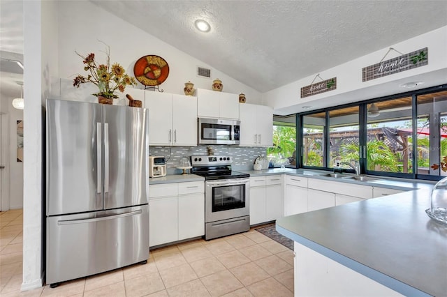 502 SE Guava Ter, Port St Lucie, FL 34983 - kitchen with appliances with stainless steel finishes, lofted ceiling, a textured ceiling, white cabinetry, and tasteful backsplash