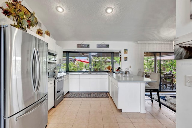 502 SE Guava Ter, Port St Lucie, FL 34983 - kitchen with stainless steel appliances, a peninsula, a textured ceiling, white cabinetry, and a kitchen bar