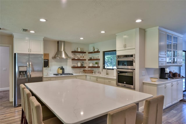 2855 SE 38th St, Ocala, FL 34480 - kitchen featuring stainless steel appliances, wall chimney exhaust hood, dark wood-style flooring, a kitchen breakfast bar, and white cabinets