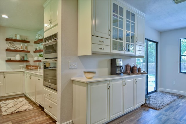 2855 SE 38th St, Ocala, FL 34480 - kitchen with light wood finished floors, double oven, glass insert cabinets, a textured ceiling, and white cabinets