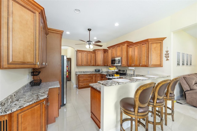 5024 SW 114th Street Rd, Ocala, FL 34476 - kitchen with appliances with stainless steel finishes, a peninsula, a ceiling fan, arched walkways, and brown cabinetry