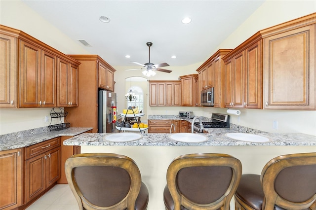 5024 SW 114th Street Rd, Ocala, FL 34476 - kitchen with appliances with stainless steel finishes, a ceiling fan, a kitchen breakfast bar, brown cabinets, and a peninsula