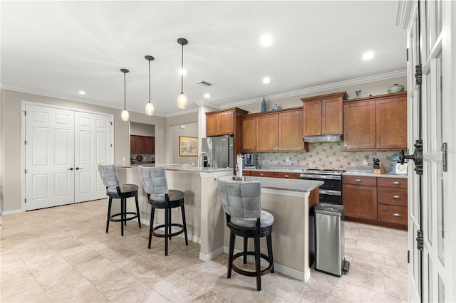 9925 SW 95th Loop, Ocala, FL 34481 - kitchen featuring stainless steel appliances, brown cabinets, under cabinet range hood, an island with sink, and crown molding