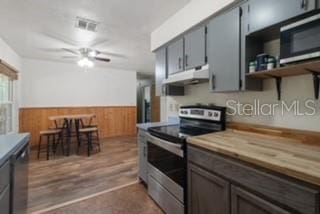 7808 E Savannah Dr, Floral City, FL 34436 - kitchen with stainless steel appliances, under cabinet range hood, wainscoting, wood walls, and a ceiling fan