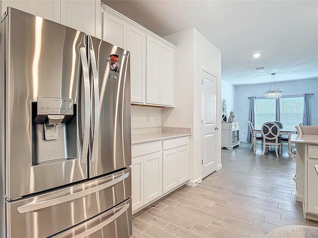 19424 SW 77th Loop, Dunnellon, FL 34432 - kitchen with stainless steel fridge with ice dispenser, light countertops, white cabinetry, light wood-style flooring, and a chandelier