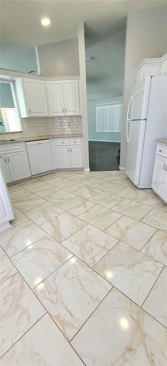 8771 SW 115th St, Ocala, FL 34481 - kitchen featuring white appliances, white cabinets, backsplash, light countertops, and light marble finish floors