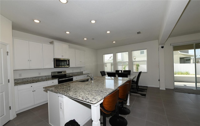 5962 SW 80th Ln, Ocala, FL 34476 - kitchen with stainless steel appliances, dark tile patterned flooring, a center island with sink, light stone countertops, and white cabinets