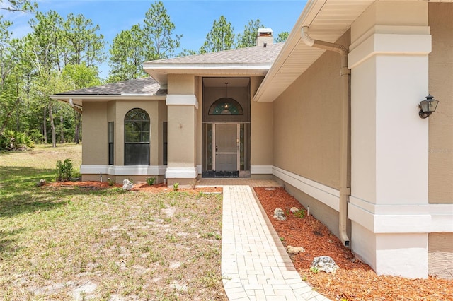 9180 SW 202nd Avenue Rd, Dunnellon, FL 34431 - view of exterior entry featuring roof with shingles, a lawn, a chimney, and stucco siding