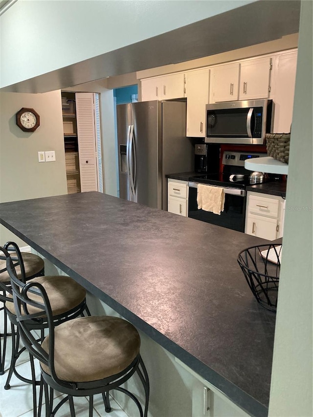 8450 SW 90th St Unit D, Ocala, FL 34481 - kitchen featuring stainless steel appliances, white cabinets, dark countertops, a breakfast bar area, and a peninsula