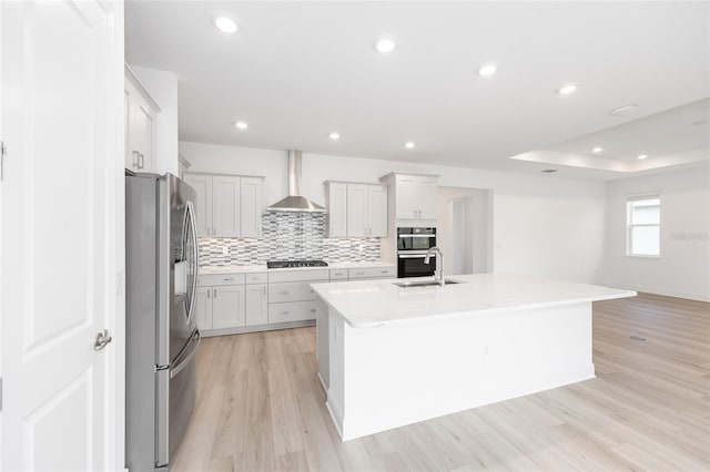 10032 SW 85th Place Rd, Ocala, FL 34481 - kitchen with stainless steel appliances, wall chimney exhaust hood, light wood-style floors, a center island with sink, and tasteful backsplash