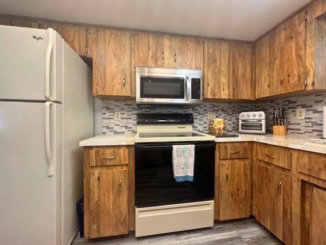 916 Jones Ave, Inverness, FL 34453 - kitchen with stainless steel microwave, freestanding refrigerator, electric range, and brown cabinetry