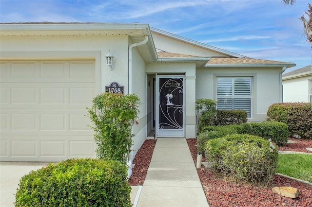 1768 SW 156th Ln, Ocala, FL 34473 - view of exterior entry with a garage, stucco siding, roof with shingles, and concrete driveway