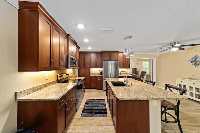 19130 NW 60th Ave, Reddick, FL 32686 - kitchen with appliances with stainless steel finishes, a kitchen bar, light wood finished floors, a kitchen island with sink, and a ceiling fan