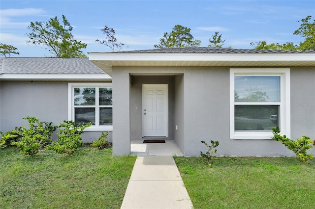 4501 SW 159th Street Rd, Ocala, FL 34473 - view of exterior entry featuring stucco siding, a lawn, and roof with shingles