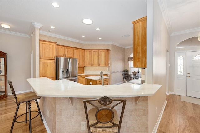 7243 SE 172nd Legacy Ln, The Villages, FL 32162 - kitchen featuring stainless steel fridge with ice dispenser, light wood-style floors, a kitchen breakfast bar, a peninsula, and ornamental molding