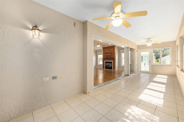 7243 SE 172nd Legacy Ln, The Villages, FL 32162 - spare room with a textured wall, light tile patterned floors, a fireplace, and a ceiling fan