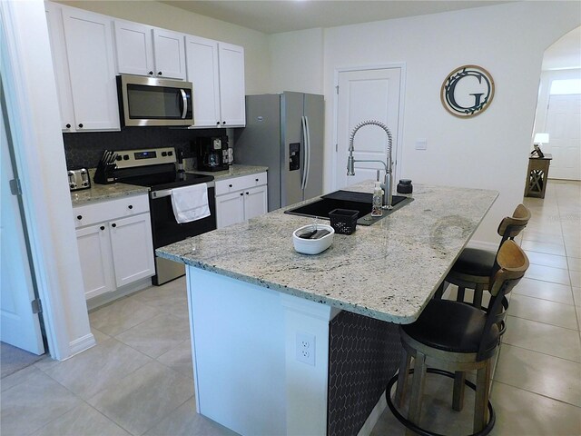 80 Hickory Course Loop, Ocala, FL 34472 - kitchen with stainless steel appliances, light tile patterned floors, white cabinets, a kitchen breakfast bar, and a kitchen island with sink