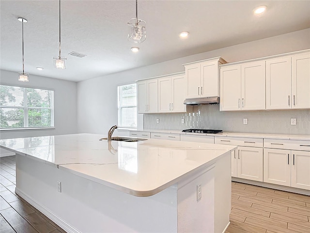 7067 SW 60th Ln, Ocala, FL 34474 - kitchen with under cabinet range hood, wood finish floors, white cabinets, stovetop, and a kitchen island with sink