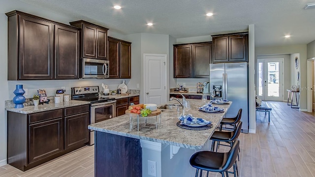 17927 NW 173rd Rd, Alachua, FL 32615 - kitchen featuring stainless steel appliances, light wood-style flooring, a breakfast bar, dark brown cabinetry, and a center island with sink