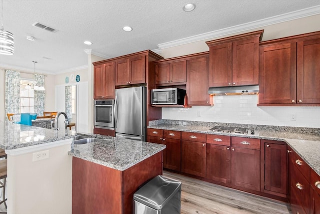 9926 SW 95th Loop, Ocala, FL 34481 - kitchen with stainless steel appliances, ornamental molding, an island with sink, light wood finished floors, and decorative backsplash