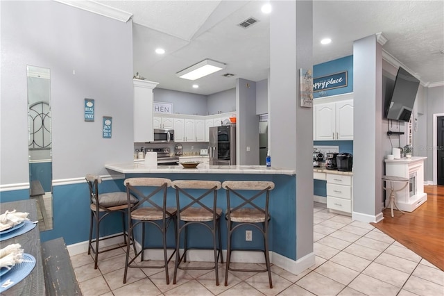 3549 SE 41st Pl, Ocala, FL 34480 - kitchen featuring stainless steel appliances, a peninsula, white cabinets, a kitchen bar, and crown molding