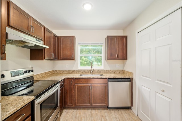 2139 NE 78th Ln, Ocala, FL 34479 - kitchen featuring appliances with stainless steel finishes, under cabinet range hood, light stone countertops, and light wood finished floors