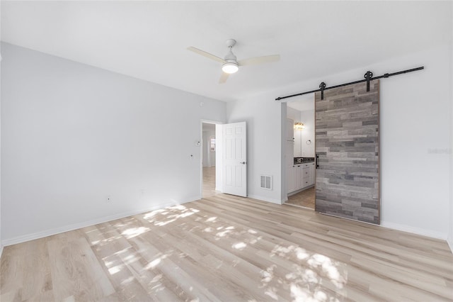 4970 NW 35th Lane Rd, Ocala, FL 34482 - unfurnished bedroom featuring a barn door, light wood-style flooring, connected bathroom, and ceiling fan