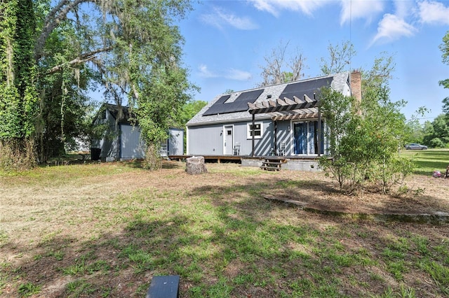 5693 Payette Ave, Keystone Heights, FL 32656 - rear view of property featuring a pergola, roof mounted solar panels, a yard, a wooden deck, and a chimney