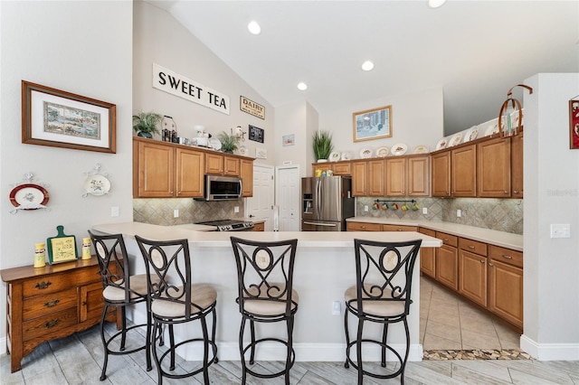 19115 SW 98th Loop, Dunnellon, FL 34432 - kitchen featuring stainless steel appliances, a breakfast bar, high vaulted ceiling, decorative backsplash, and brown cabinets