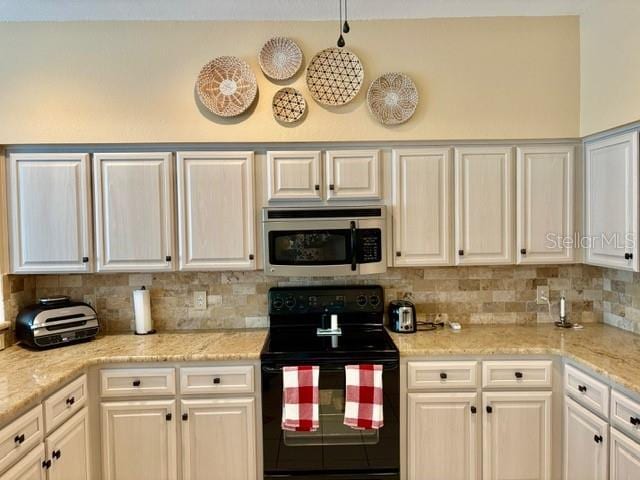 19480 SW 100th Loop, Dunnellon, FL 34432 - kitchen with stainless steel microwave, black range with electric stovetop, backsplash, white cabinetry, and light stone counters