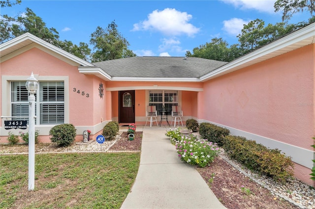3453 SE 147th Ln, Summerfield, FL 34491 - doorway to property with stucco siding, a porch, a lawn, and roof with shingles