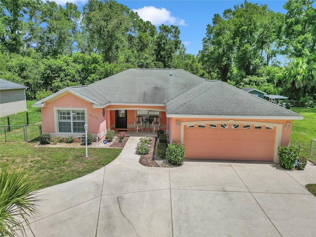 3453 SE 147th Ln, Summerfield, FL 34491 - view of front facade featuring driveway, stucco siding, a garage, view of scattered trees, and a shingled roof