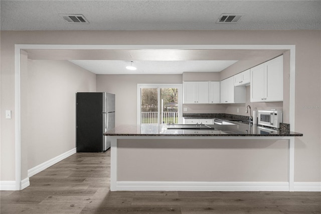 6021 NW 54th Ter, Ocala, FL 34482 - kitchen with freestanding refrigerator, a peninsula, dark stone countertops, white cabinets, and white microwave
